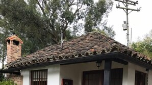 Una pequeña casa de un solo piso con techo de tejas, una chimenea de ladrillo y un porche con una mecedora.