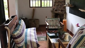 Una habitación acogedora con un banco de madera, una mesita con velas, una chimenea de ladrillo y una ventana con persianas.