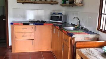 Una cocina con armarios de madera, piso de baldosas, microondas y un lavamanos.