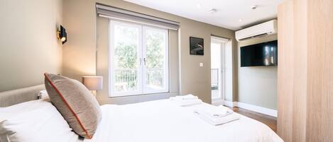 Una habitación de hotel moderna con una cama grande, un televisor de pantalla plana y una ventana con vistas a zonas verdes.