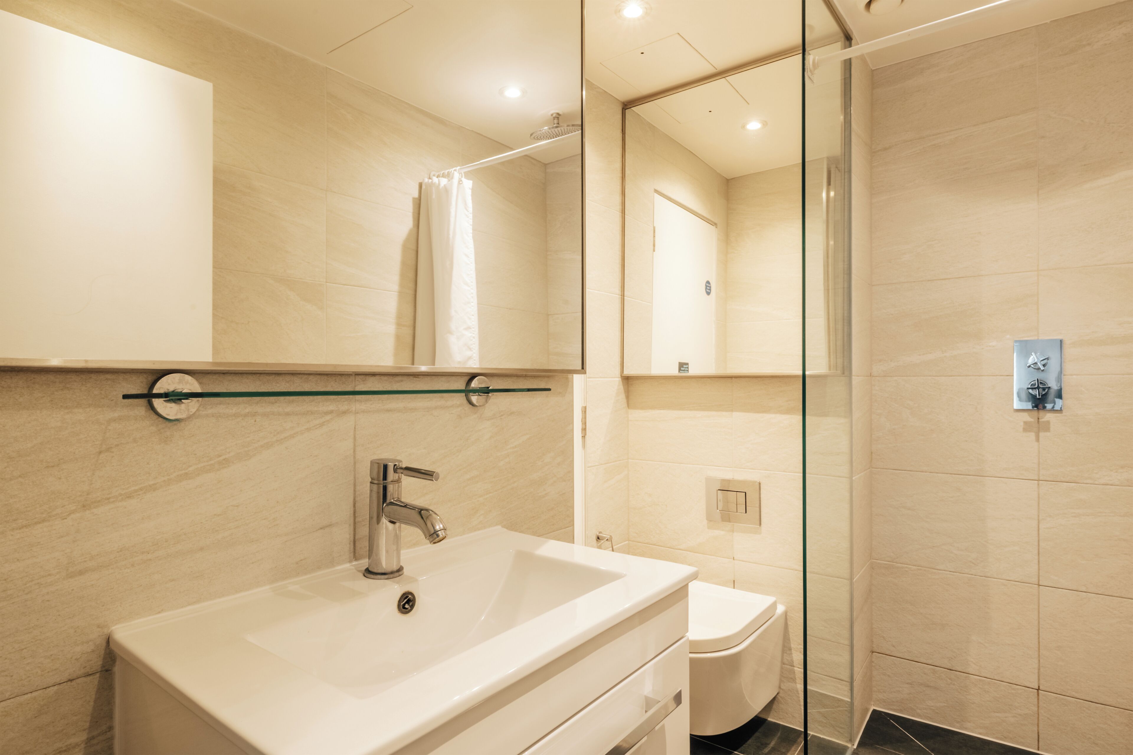 Une salle de bain moderne avec un grand miroir, un lavabo, une douche à parois de verre et des toilettes.