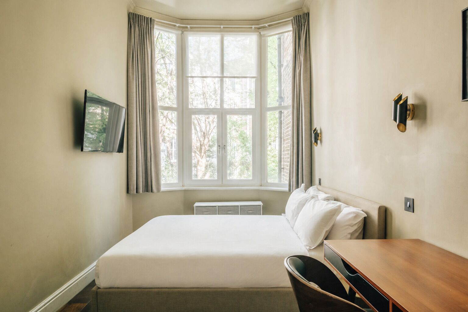 Un dormitorio con un ventanal grande, una cama, un escritorio y una silla.
