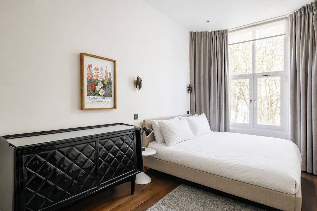 Un dormitorio con cama, cómoda, ventana con cortinas e imagen colgada en la pared.