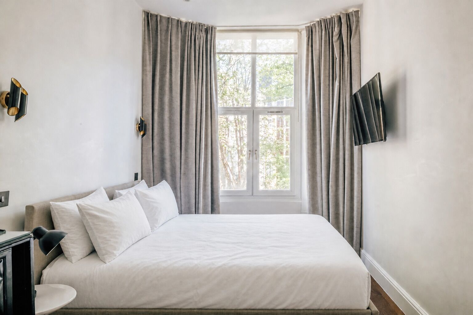A hotel room with a bed, a desk, a chair, a TV, and a window with curtains.