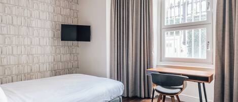 Ein Hotelzimmer mit Bett, Schreibtisch, Stuhl, Fernseher und einem Fenster mit Vorhängen.