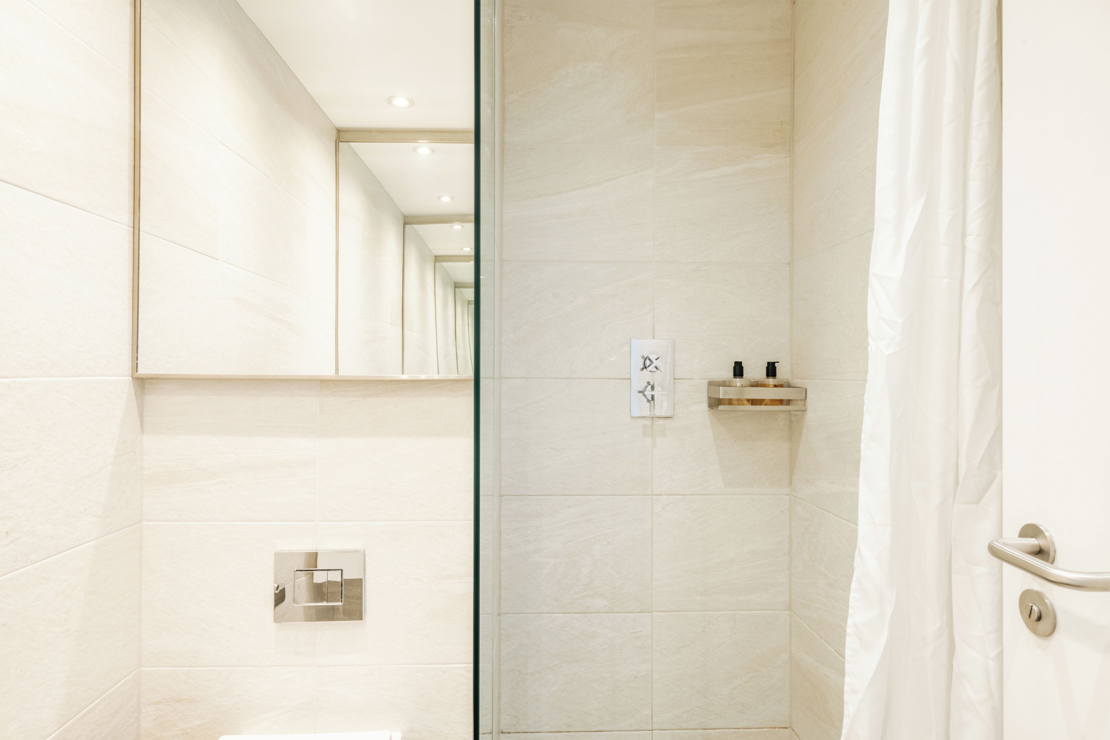 A modern bathroom with a glass shower door, a mirror, and a small shelf with toiletries.