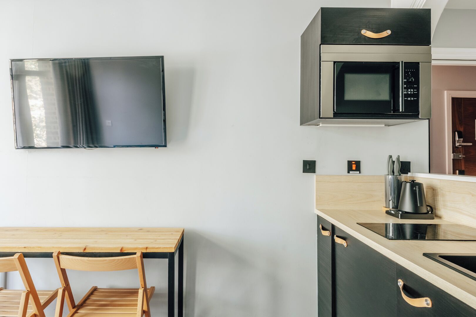 Egy modern konyha, amelyben van egy síkképernyős televízió, egy mikrohullámú sütő, egy kávéfőző, valamint egy fából készült étkezőasztal székekkel.