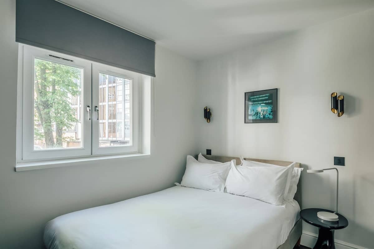 Un dormitorio con una cama, dos mesitas de noche, un ventanal y un cuadro colgado en la pared.