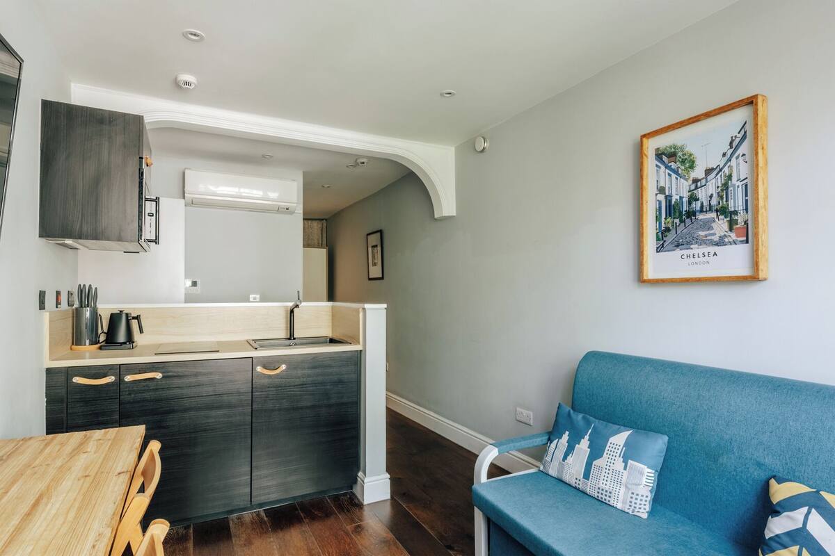 Una cocina moderna con armarios oscuros, una mesa de comedor de madera y un sofá azul con cojines alusivos a la ciudad.