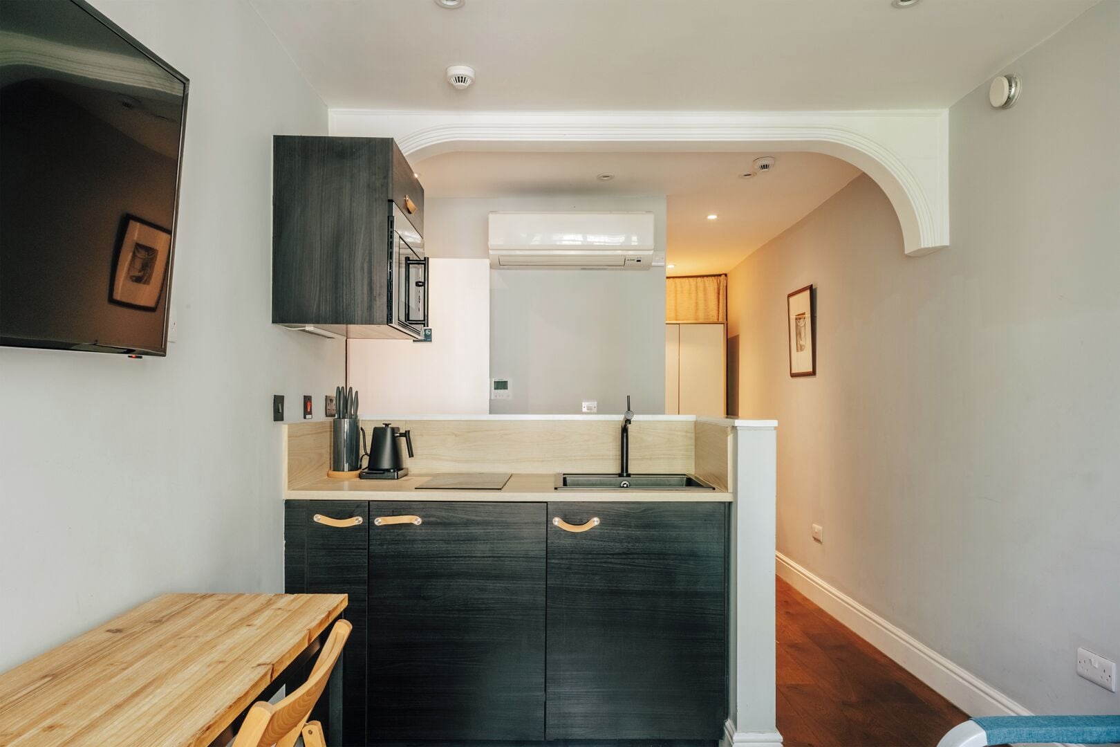Une cuisine moderne avec des meubles de couleur sombre, une table en bois et un four encastré.