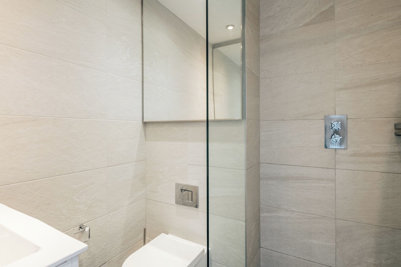 A modern bathroom with a glass shower enclosure, a white sink, and a mirror.