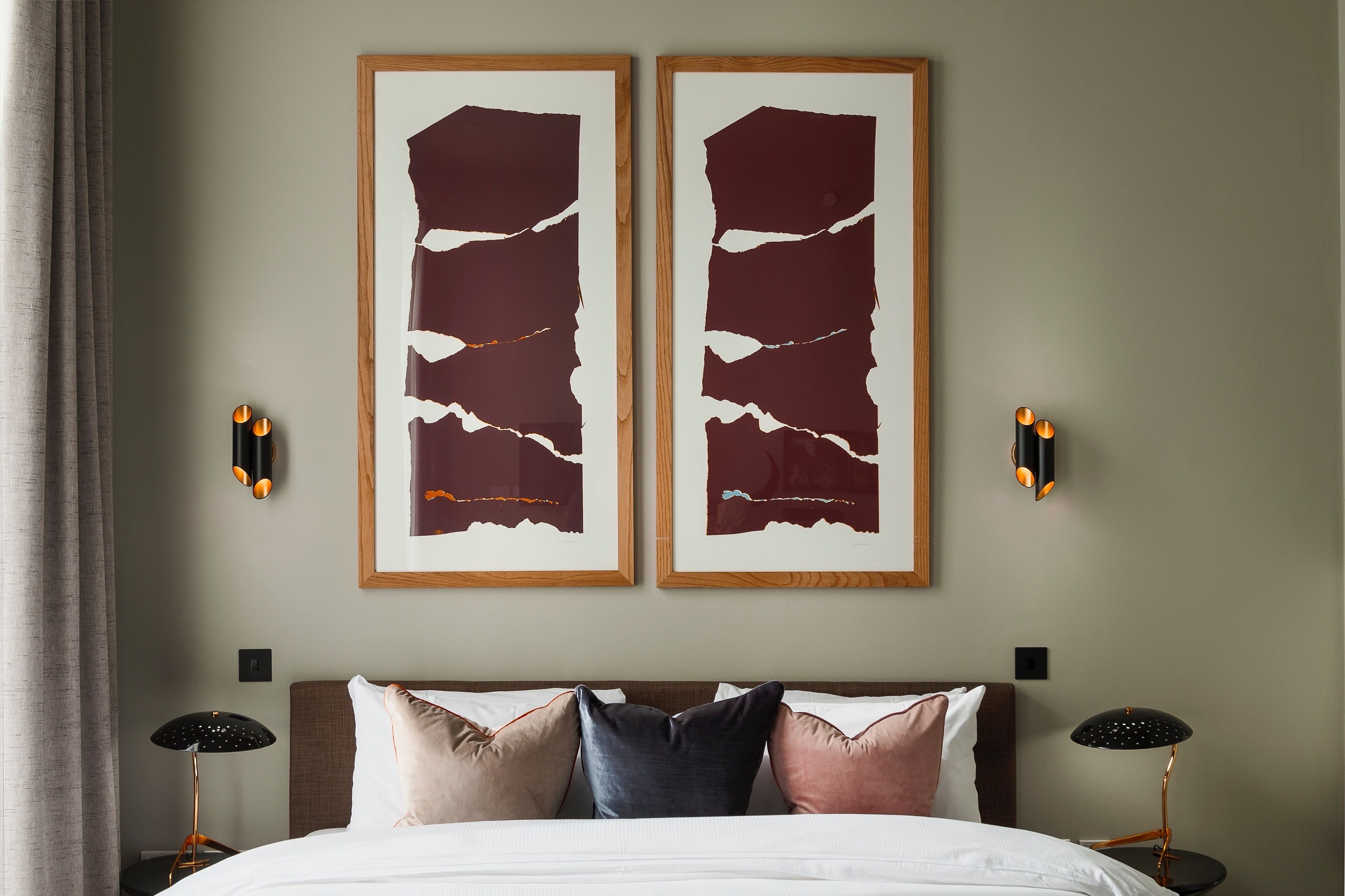 A hotel room with a bed, two wall-mounted abstract paintings, and two floor lamps.