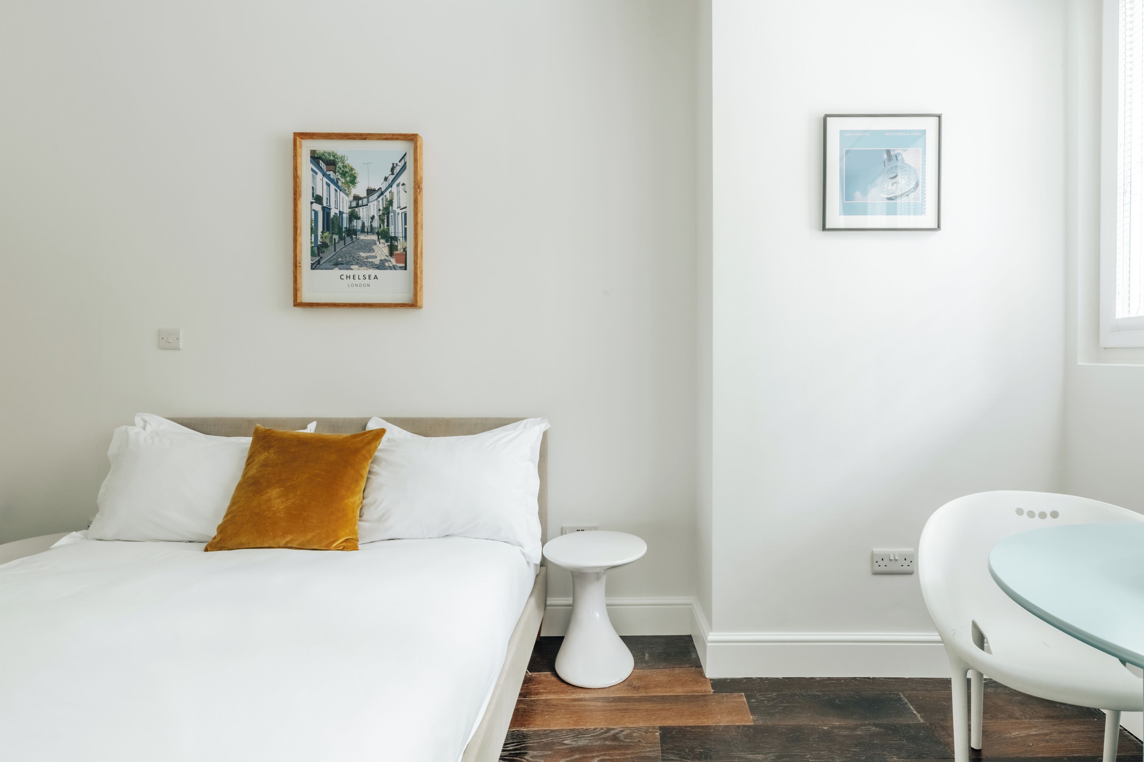 A hotel room with a bed, a small round table, a chair, a wall-mounted picture, and a window.