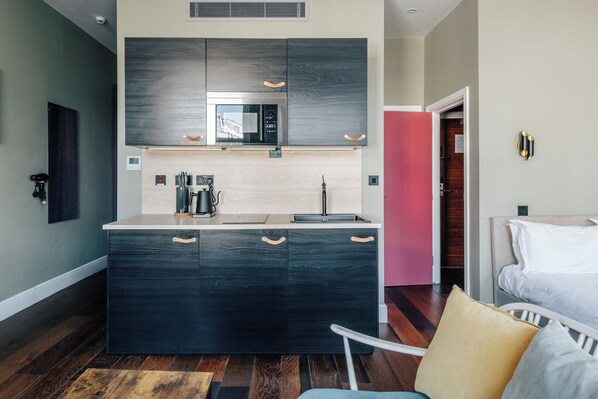 A modern kitchen with dark cabinetry, a built-in microwave, and a coffee maker. - The Knaresborough by Nestor (London)