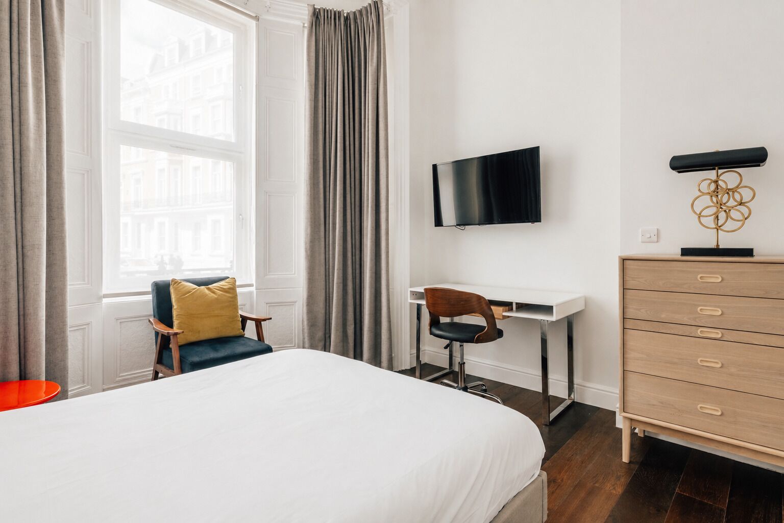 Et hotelværelse med seng, skrivebord, stol, fjernsyn og kommode.