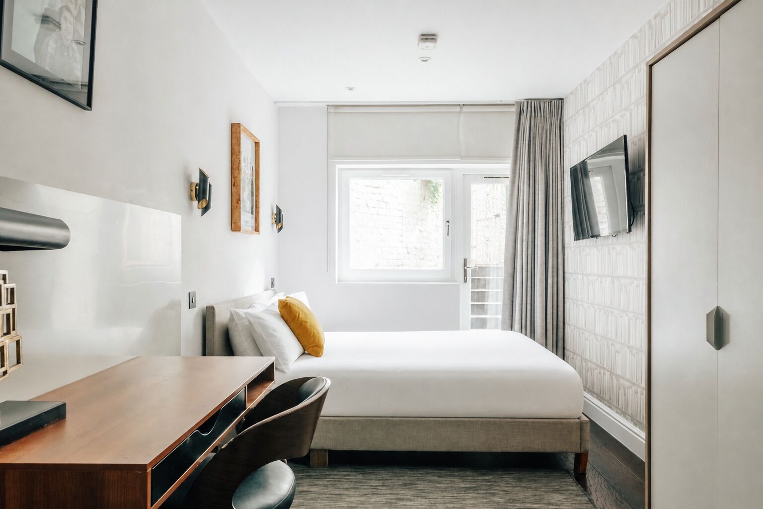 A hotel room with a bed, a desk, a chair, a TV, and a window with curtains.
