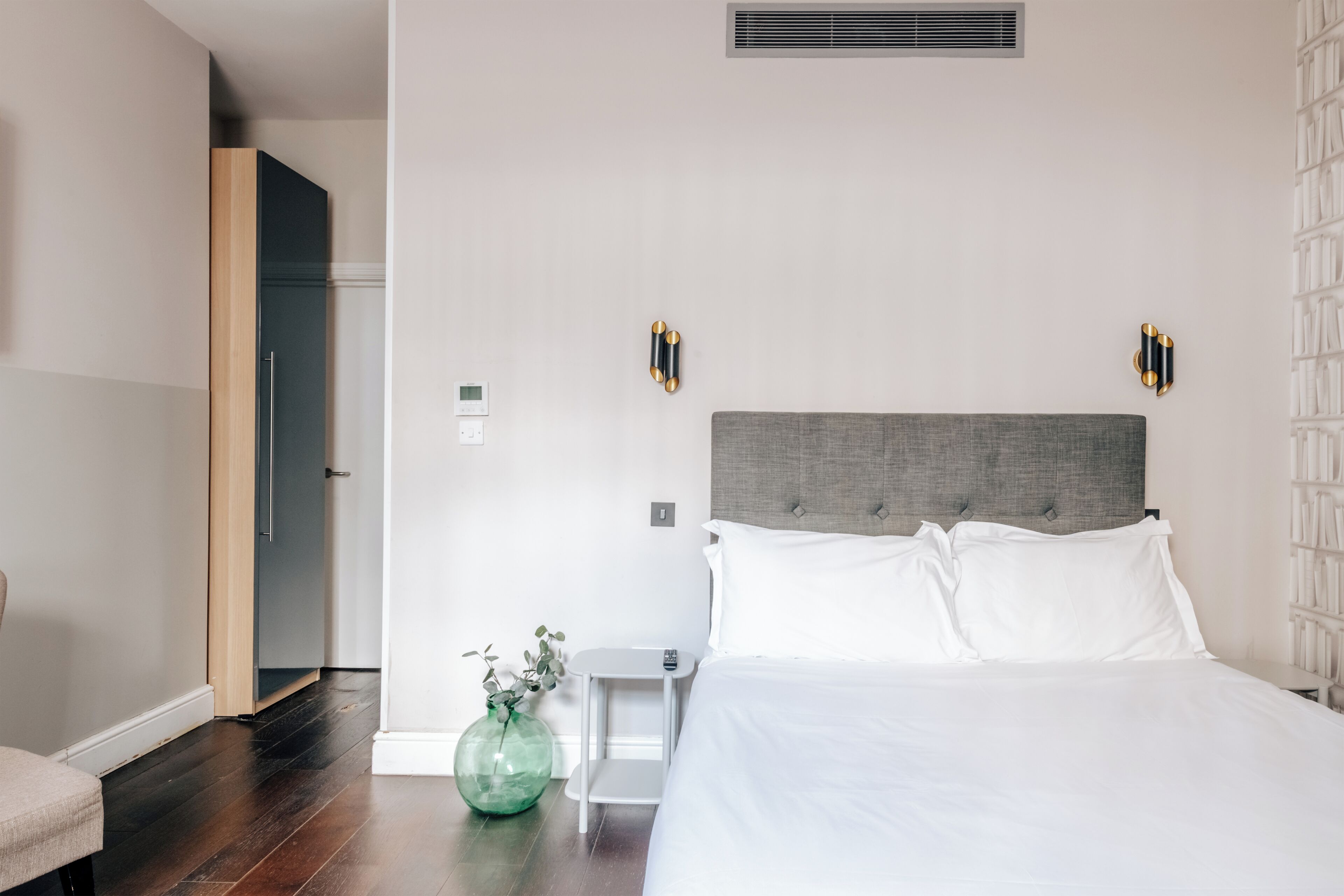 A hotel room with a bed, bedside table, and a vase with a plant.