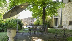 An outdoor patio with a table and chairs, a large planter, and a stone building in the background. - Mas du Crès (Galargues)