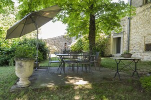 Un patio al aire libre con una mesa y sillas, una jardinera grande y un edificio de piedra al fondo.