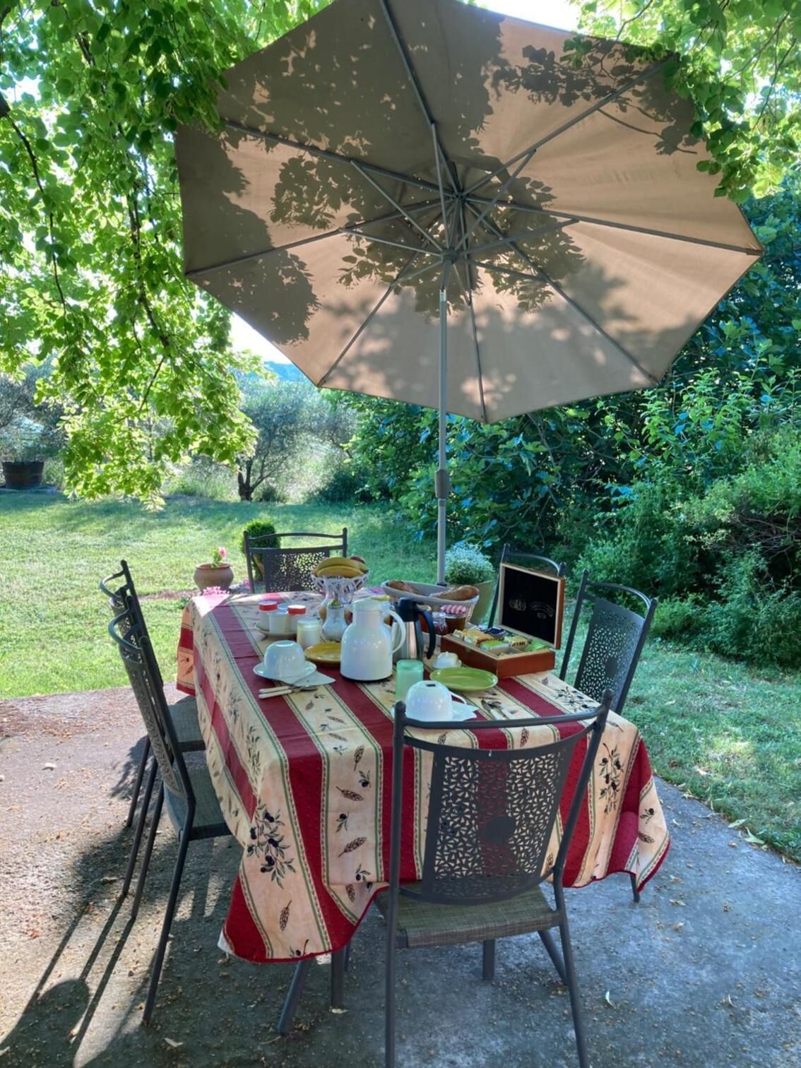 Un área de comedor al aire libre con una mesa bajo un gran paraguas, rodeada de sillas y vistas a un jardín.