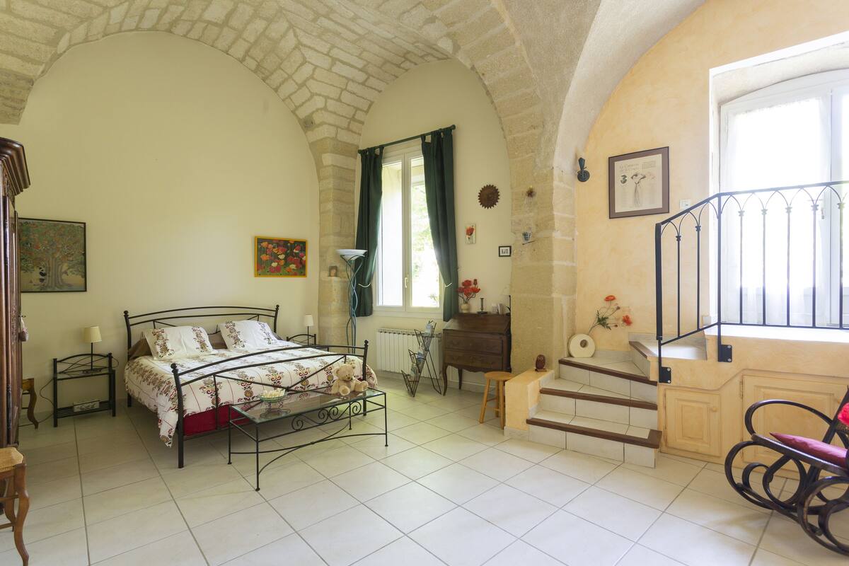 A bedroom with a bed, a dresser, a chair, a window, and a staircase.
