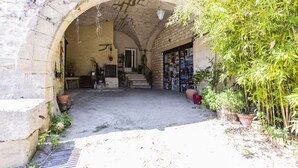 An arched stone entrance to a building with a staircase leading inside, surrounded by potted plants and a small outdoor seating area. - Mas du Crès (Galargues)