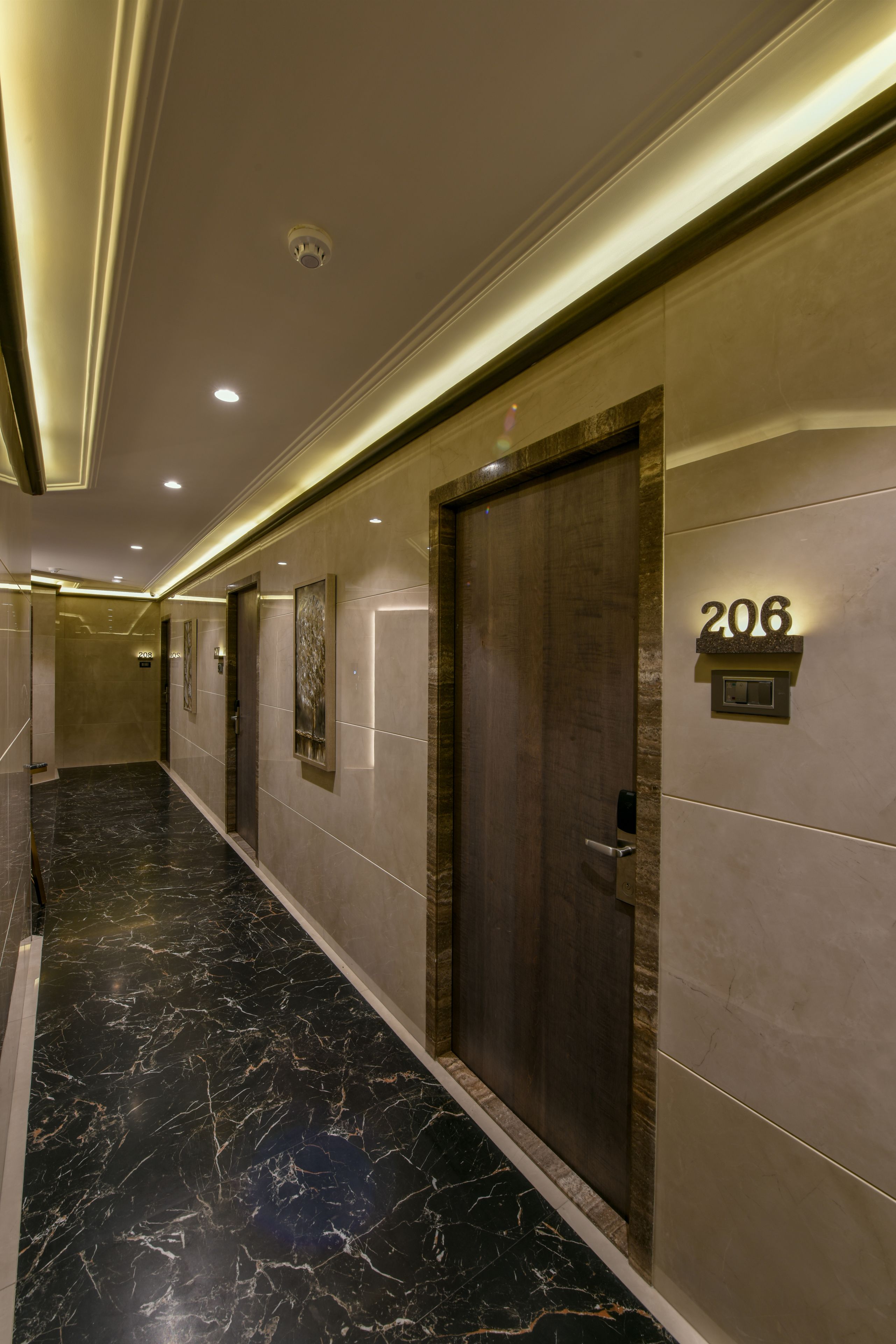 A hallway with a marble floor, a wooden door, and a wall-mounted number sign indicating room 206.