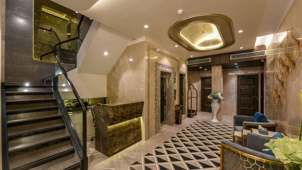 A lobby with a geometric patterned floor, a reception desk, a staircase, and a seating area with a vase of flowers. - Hotel Orient Regency (Mumbai)