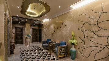 A lobby with a geometric patterned floor, a reception desk, a seating area with sofas, a decorative vase, and a wall with abstract designs.