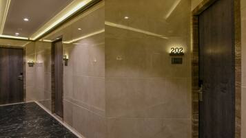 Um corredor com piso de mármore, teto com iluminação embutida e portas numeradas.