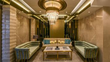 A luxurious lobby with a central sofa, two armchairs, a coffee table, and a chandelier.