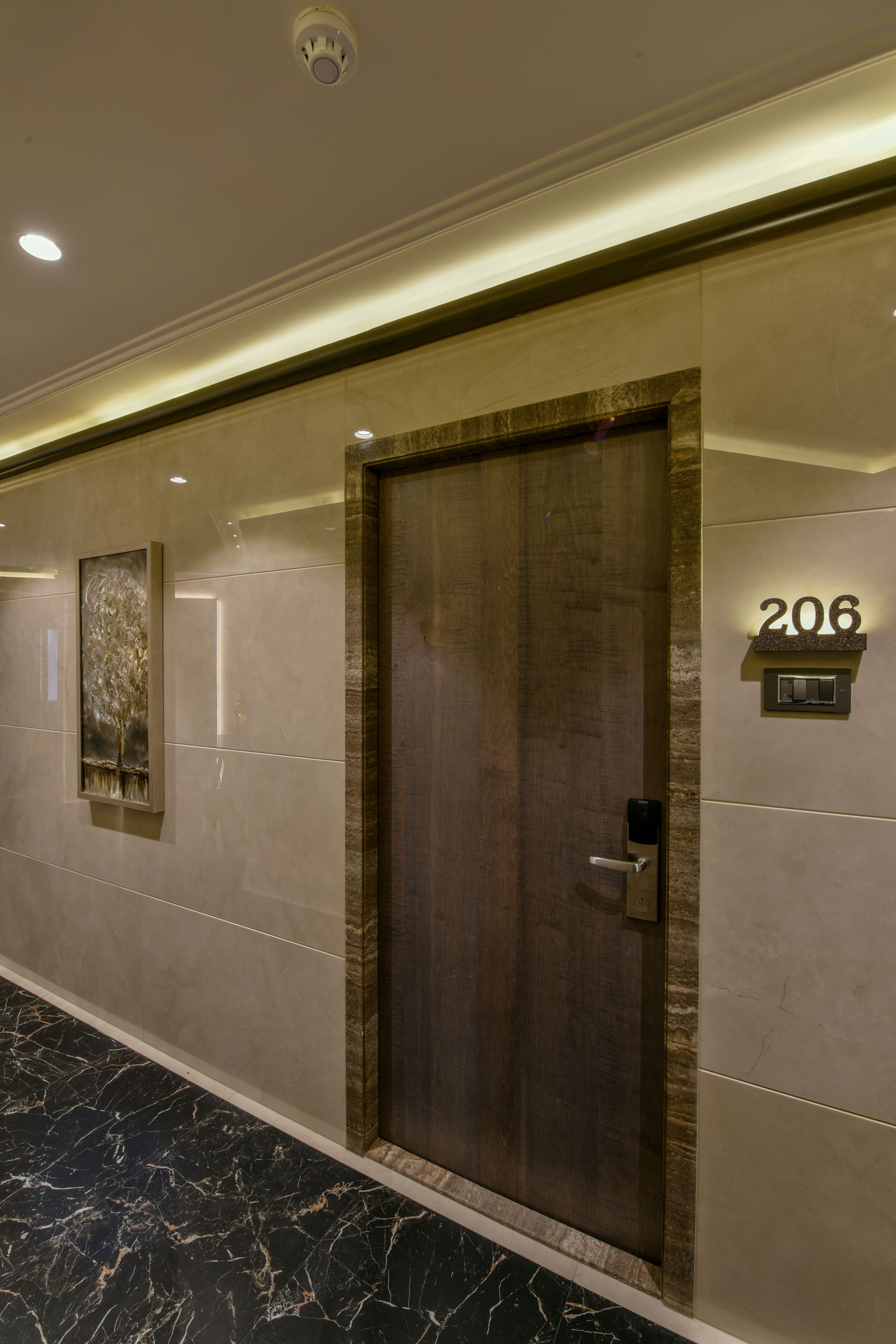 A hallway with a wooden door, a number sign '206', and a wall-mounted light fixture.