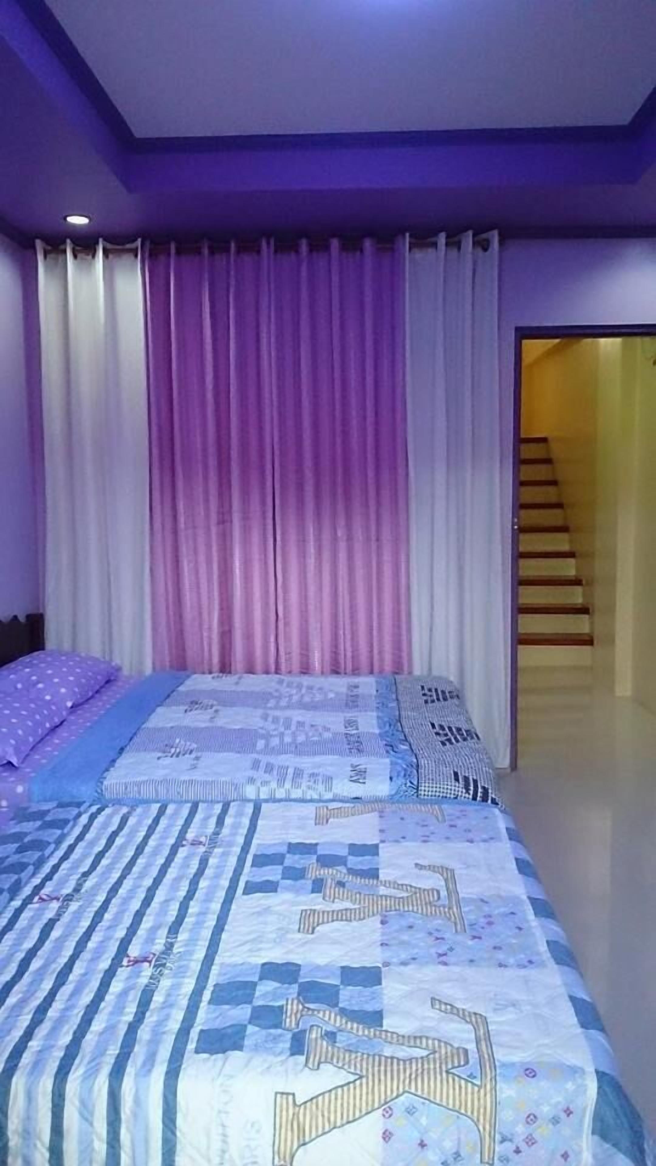 A bedroom with a bed, curtains, and a staircase leading to another room.