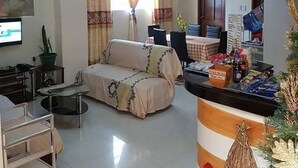 Una sala de estar con un sofá, un televisor, una zona de comedor con una mesa y sillas, una encimera de cocina con objetos, y un árbol de Navidad.