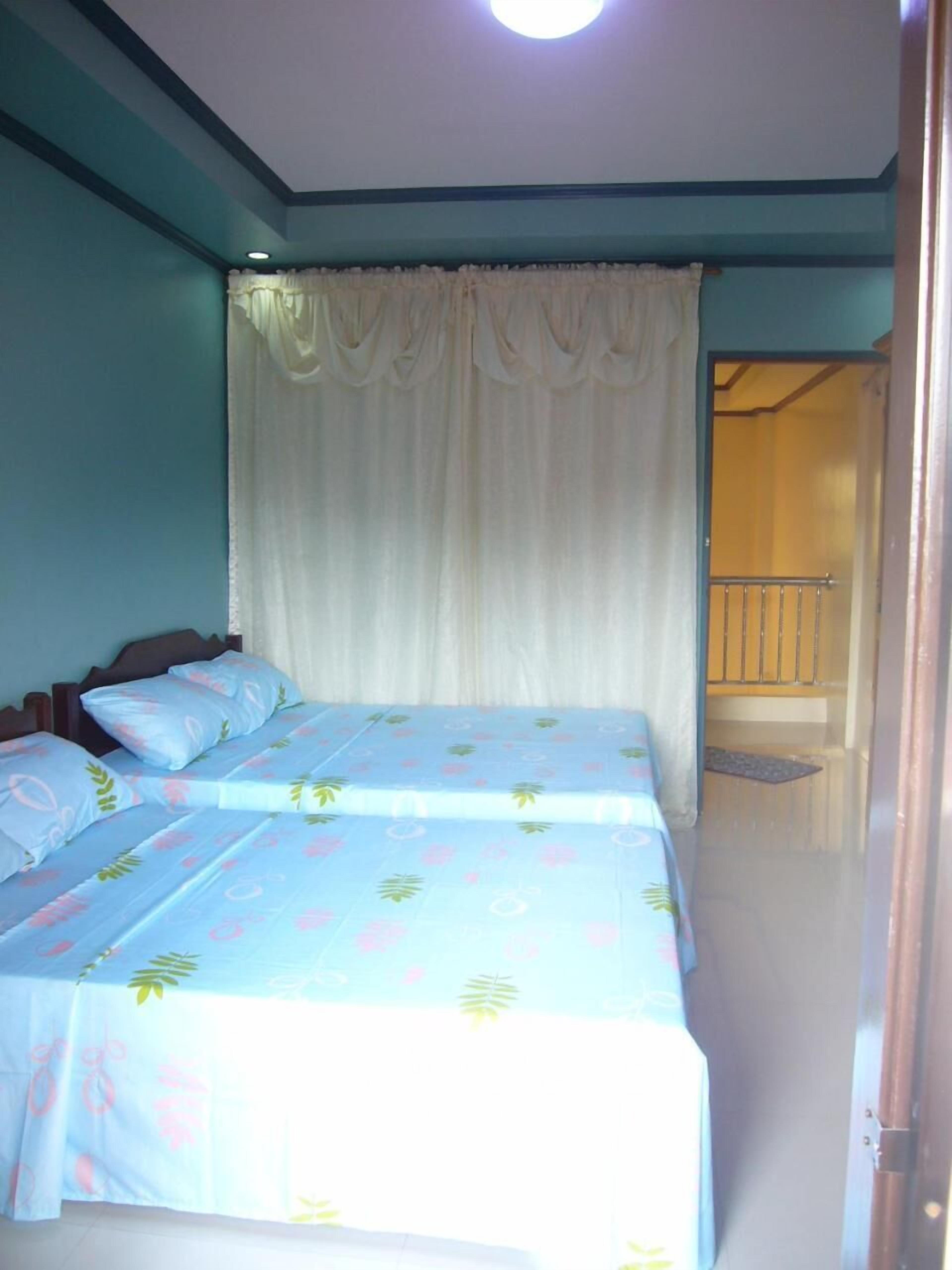 A bedroom with two beds, a white curtain, and a view of a balcony.