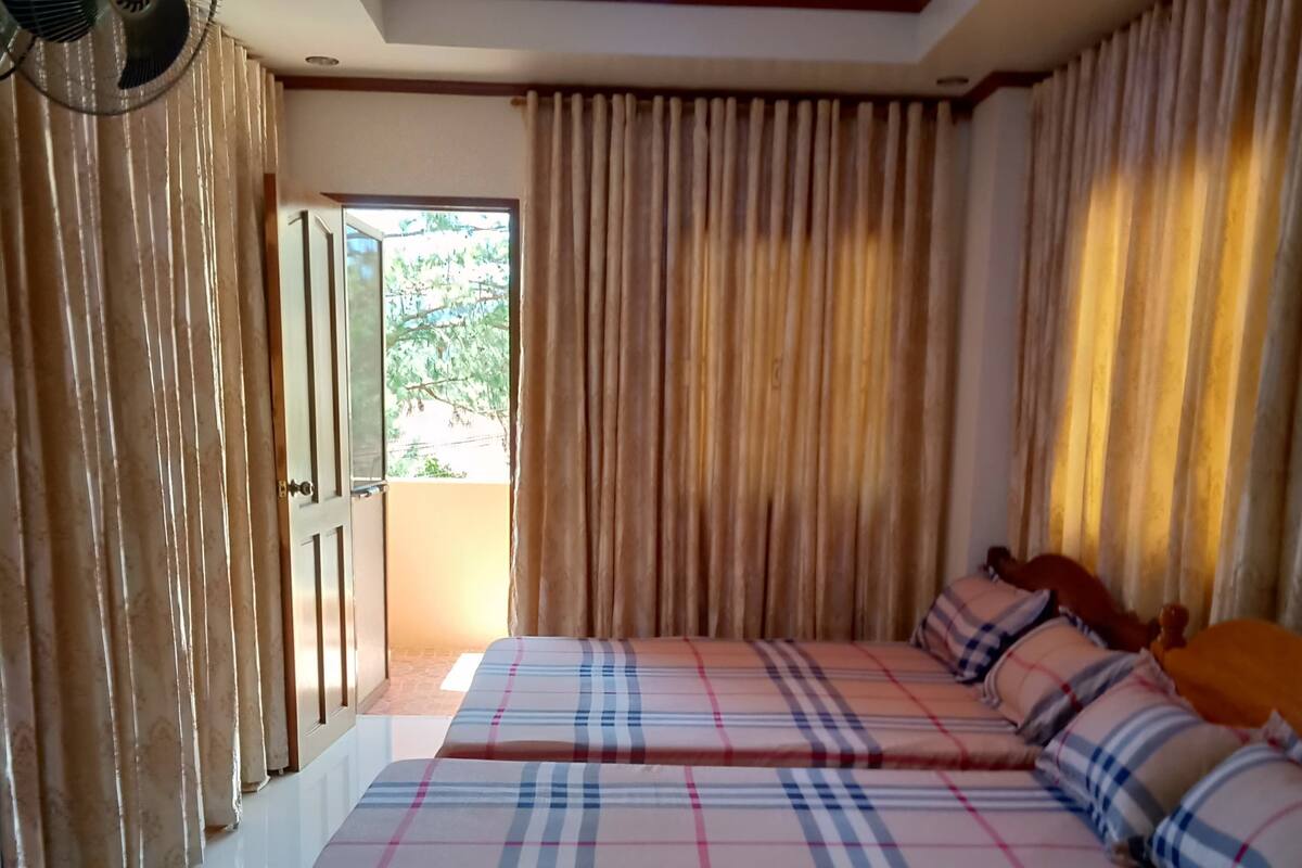 A bedroom with two beds, a ceiling fan, and a view of greenery outside.