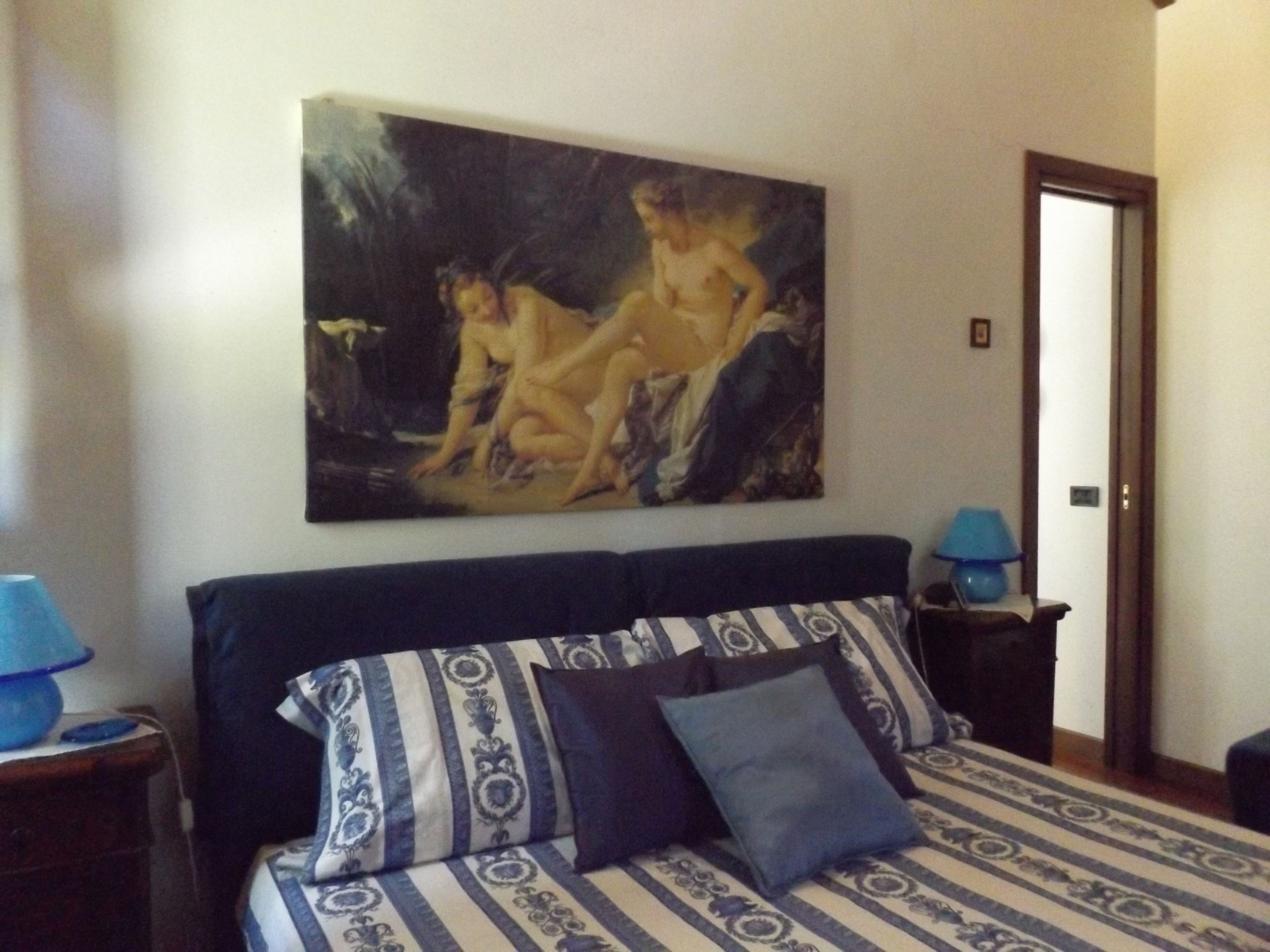 A bedroom with a bed, a painting, and two bedside tables with lamps.