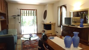 A living room with a sofa, a coffee table, and a TV. There is a door leading outside and a mirror on the wall. - Villa delle Sirene (Garda)