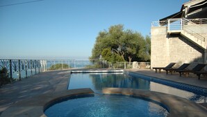 A swimming pool with a view of the sea, a stone building with a balcony, and lounge chairs. - Résidence Capicciolo (Olmeto)