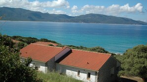 A coastal building with a red-tiled roof, surrounded by greenery and overlooking a clear blue sea with distant mountains. - Résidence Capicciolo (Olmeto)