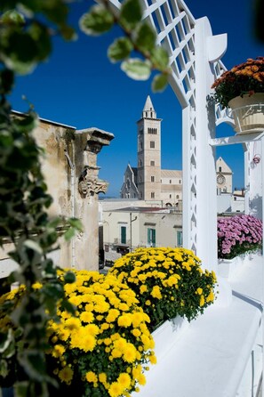 Une structure blanche ornée d’un motif en treillis, un bâtiment doté d’une tour, et des fleurs jaunes au premier plan.