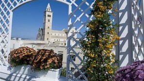Une structure blanche en forme de treillis ornée de fleurs, avec un bâtiment doté d’une tour en arrière-plan.