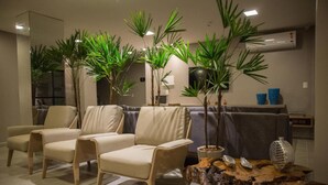 A modern living room with three beige armchairs, a grey sofa, and a coffee table with decorative items. - Amenit Hotel (Maceió)