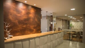 A modern reception area with a wooden counter, a glass partition, and a seating area with tables and chairs. - Amenit Hotel (Maceió)