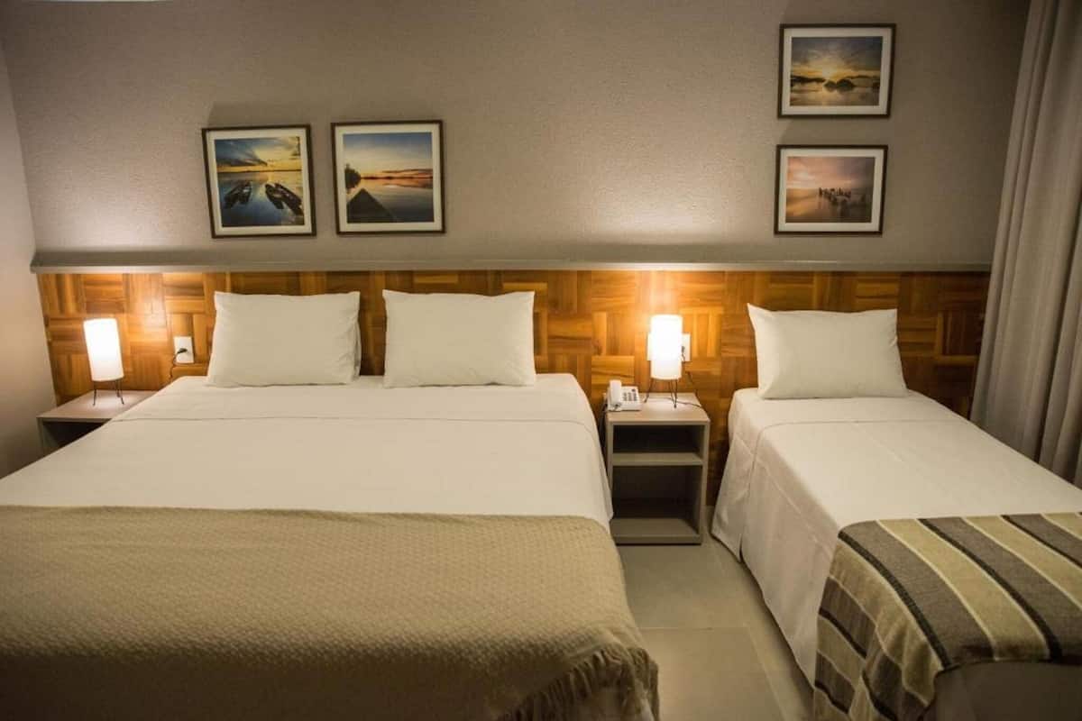 A hotel room with two beds, a wooden headboard, bedside lamps, and framed pictures on the wall.
