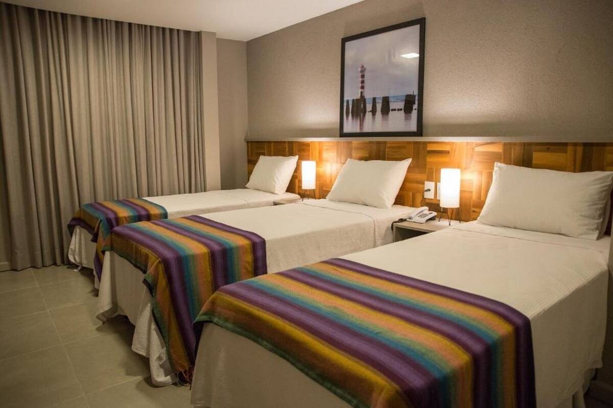 A hotel room with two beds, a wooden headboard, a framed picture on the wall, and a curtain.
