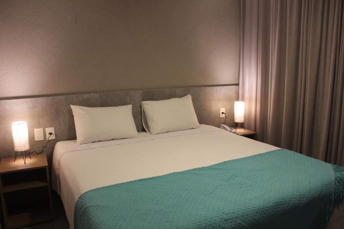 A hotel room with a bed, two bedside lamps, a nightstand, and a curtain.