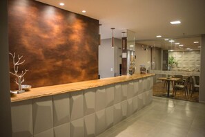 Una recepción moderna con mostrador de madera, separador de vidrio y zona de estar con mesas y sillas.