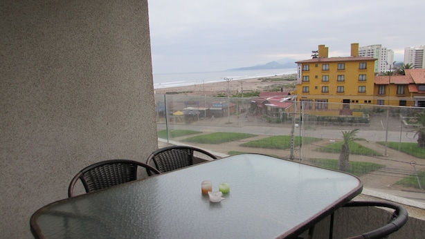 A balcony with a table and chairs, overlooking a beach and buildings. - 9.- HNA Mirador El Faro (La Serena)