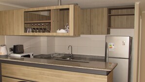 A modern kitchen with wooden cabinets, a stainless steel refrigerator, a sink, and a bar area with stools. - 9.- HNA Mirador El Faro (La Serena)